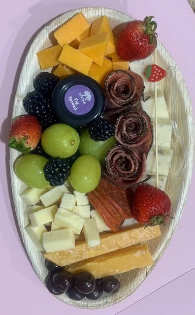 A cheese and fruit platter with strawberries, green grapes, blackberries, cheeses, slices of meats, cheddar cheese, dark cherries, and a small container of spread.