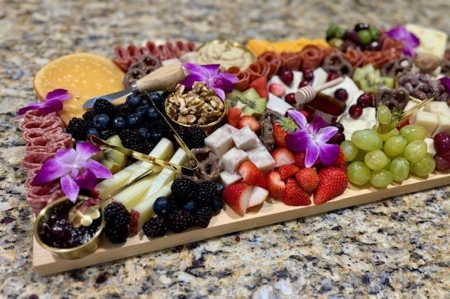 Charcuterie board with cheese, grapes, strawberries, blackberries, crackers, and edible flowers on a granite countertop.