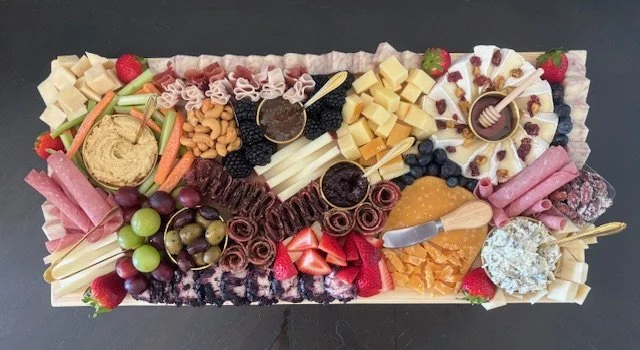 An assorted charcuterie board with cheeses, meats, fruits, crackers, and condiments.