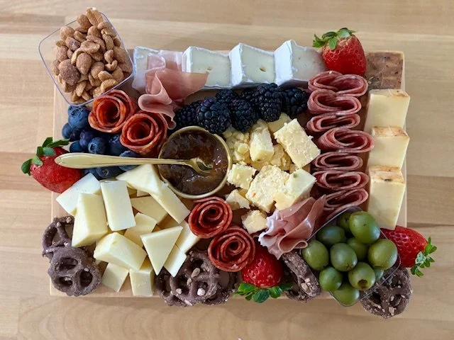 Cheese and fruit platter with strawberries, grapes, blackberries, and an assortment of cheeses, meats, and nuts on a wooden surface.