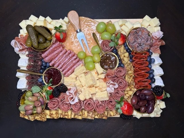 A charcuterie board with cheeses, meats, grapes, strawberries, blueberries, blackberries, pickles, olives, and various crackers and spreads.