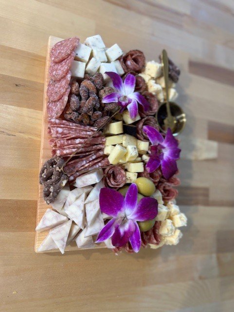 Charcuterie board with assorted cheeses, cured meats, grapes, and edible flowers on a wooden surface.