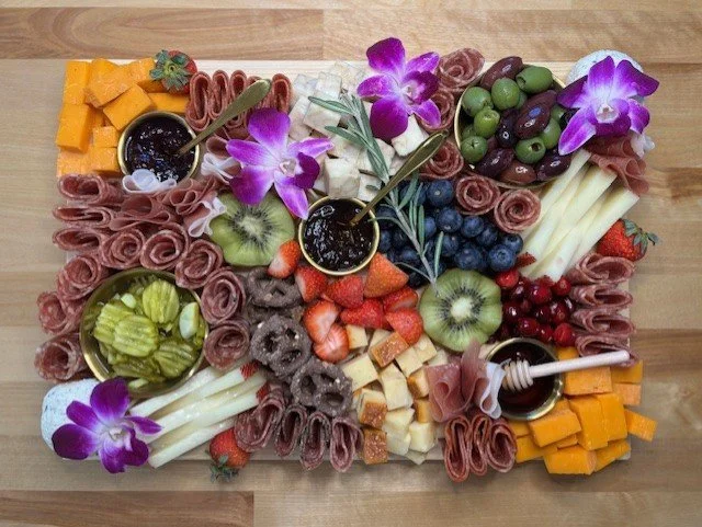Charcuterie board with cheeses, fruit, vegetables, and orchids.
