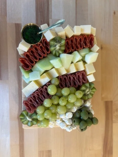 Charcuterie board with cured meats, cheese cubes, grapes, and melon.
