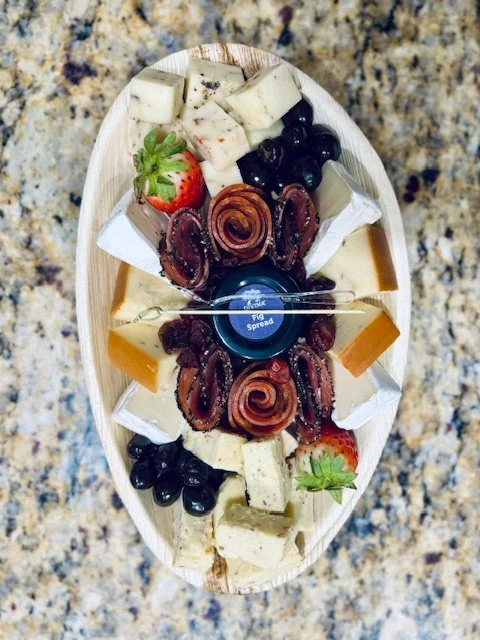 A cheese and meat platter with strawberries, black olives, and cheese cubes on a wooden serving tray.