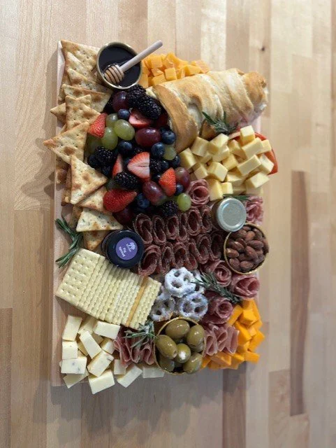 Charcuterie board with cheese, crackers, strawberries, grapes, blackberries, blueberries, prosciutto, honey, jams, and nuts on a wooden surface.