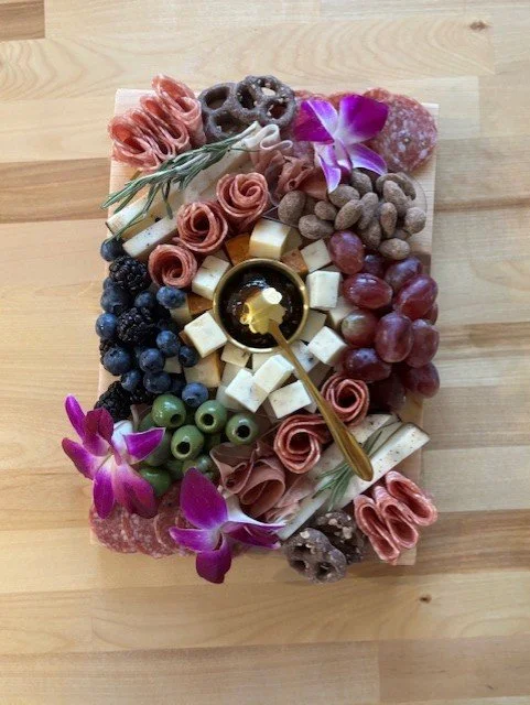 Charcuterie board with cheese, grapes, blackberries, olives, flowers, and crackers.