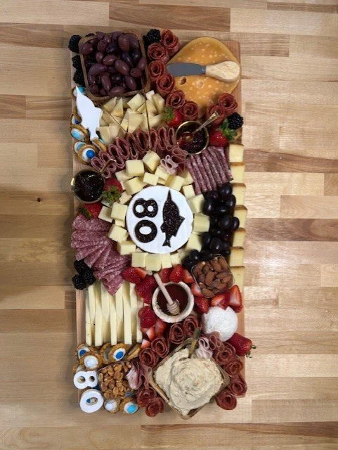 Charcuterie board with grapes, cheese, crackers, olives, almonds, strawberries, strawberries and blueberries, and a circular treat with the number 80 and a fish illustration, celebrating an 80th birthday.