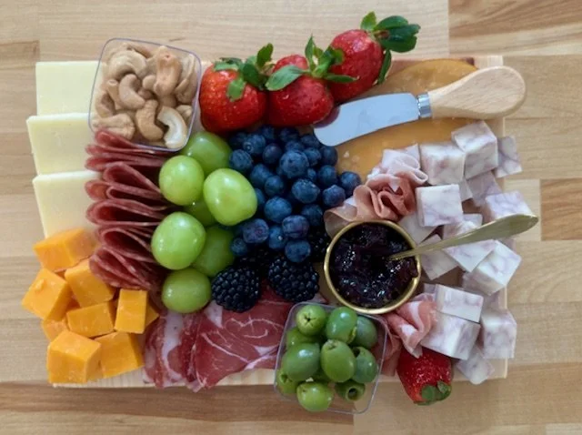 A charcuterie platter with cheese, meats, grapes, strawberries, blackberries, blueberries, walnuts, and a jar of jam on a wooden surface.