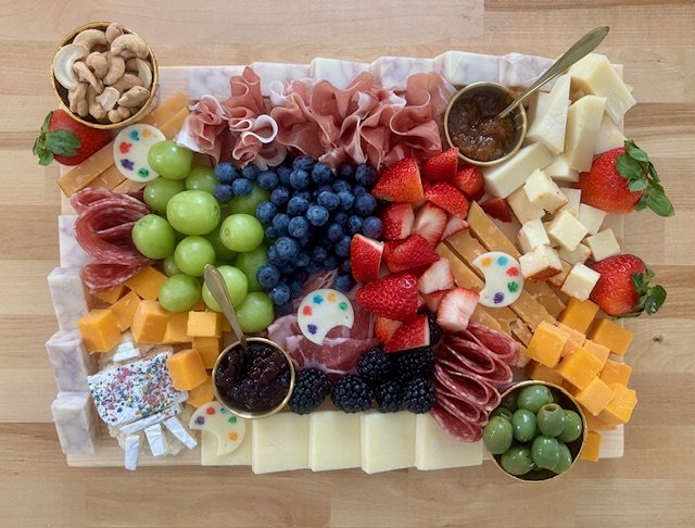 A cheese and fruit platter with grapes, strawberries, blueberries, blackberries, cheeses, cured meats, crackers, and olives on a wooden table.