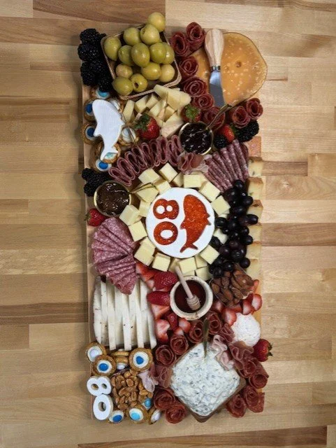 Large charcuterie and cheese board with grapes, berries, sliced meats, cheeses, crackers, nuts, and dipping sauces on a wooden surface.