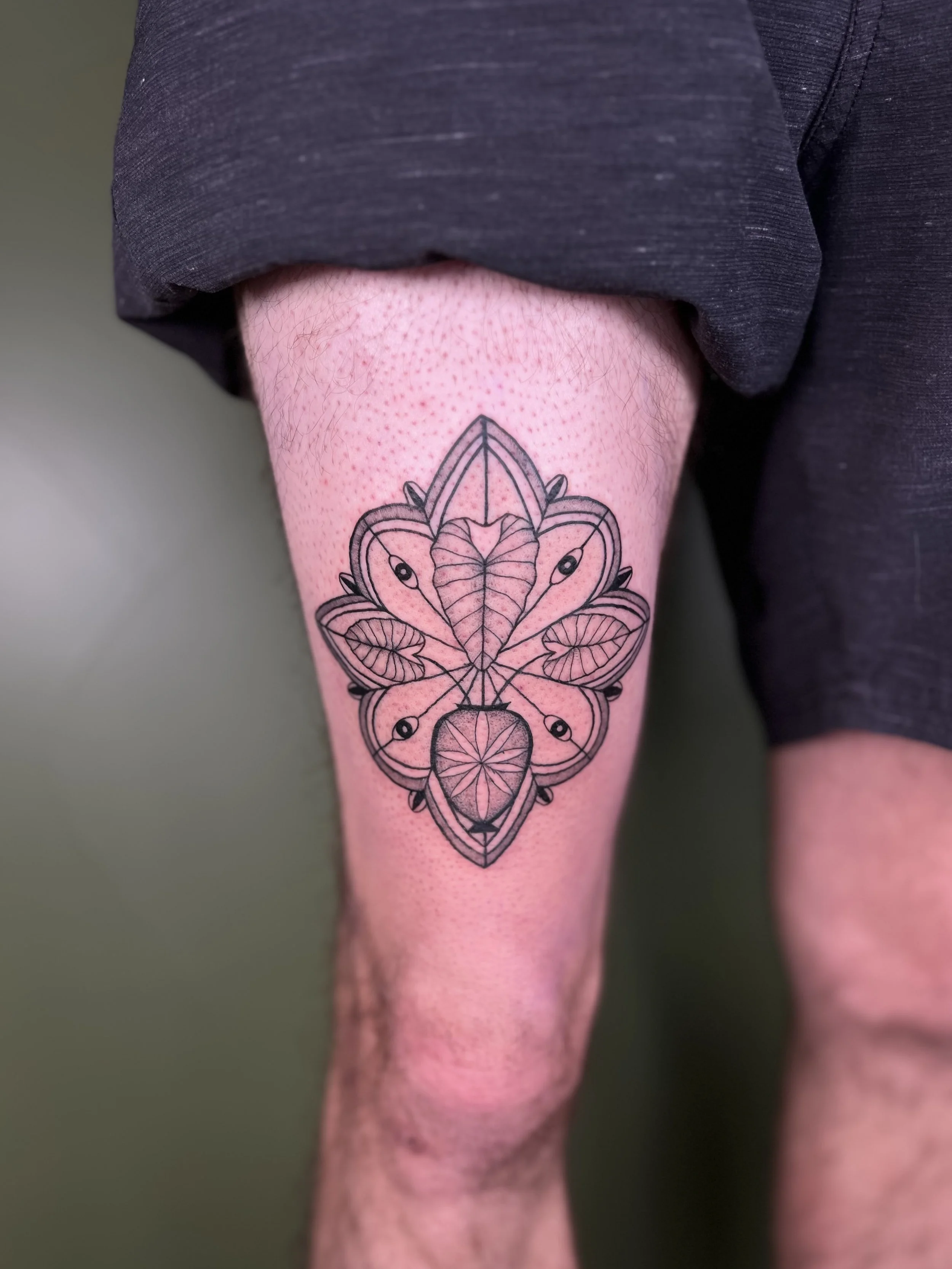 A tattoo on a person's calf features a stylized geometric butterfly with intricate line work and leaf details inside its wings.