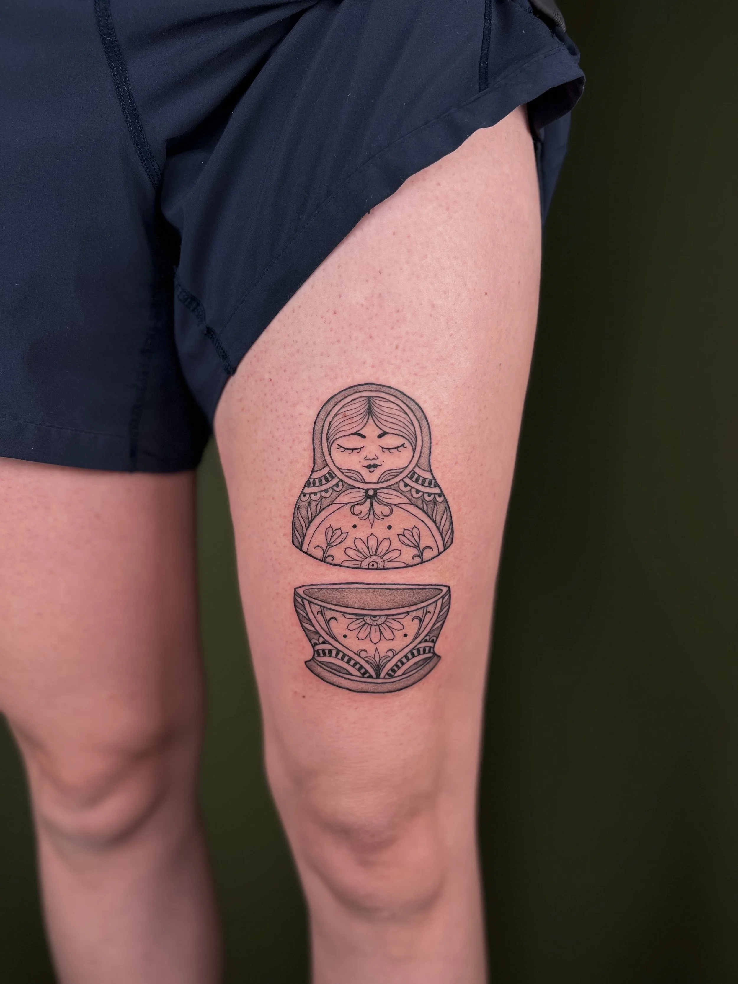 Tattoo of a matryoshka doll on a person's thigh, with intricate patterns and floral designs.