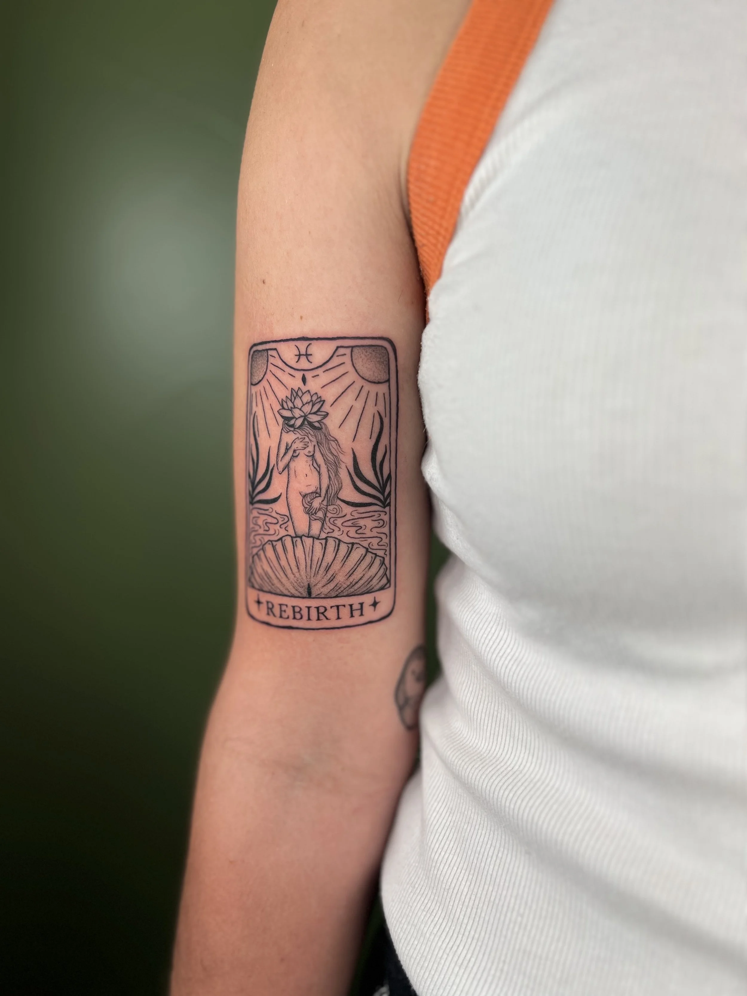 Tattoo of a reclining woman with a flower on her head, surrounded by plants, with the word 'REBIRTH' at the bottom.