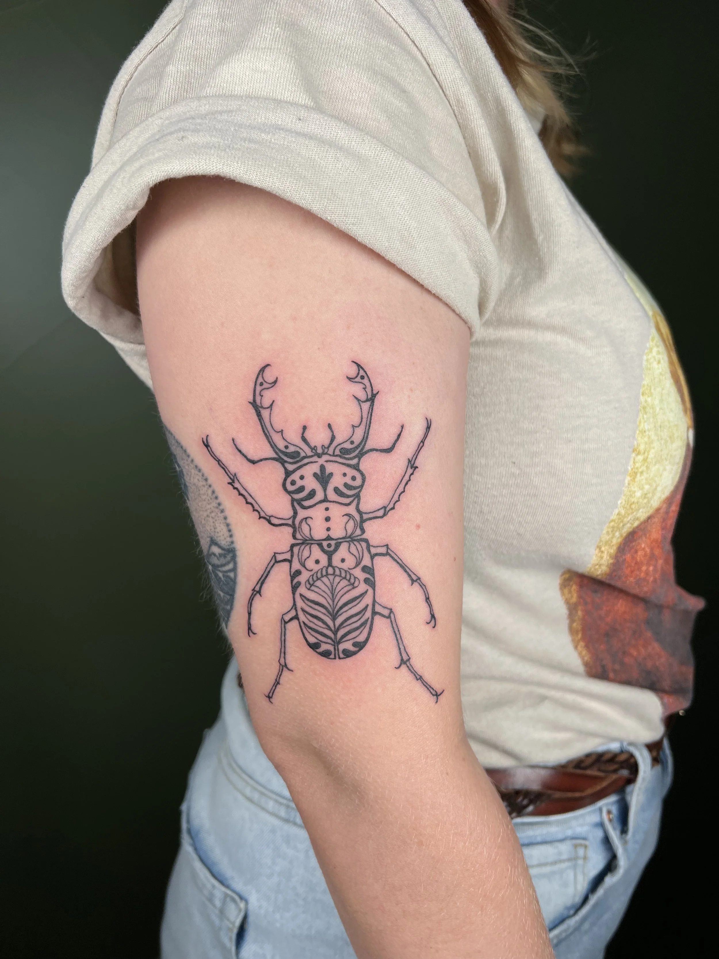 Tattoo of a detailed beetle on woman's upper arm.