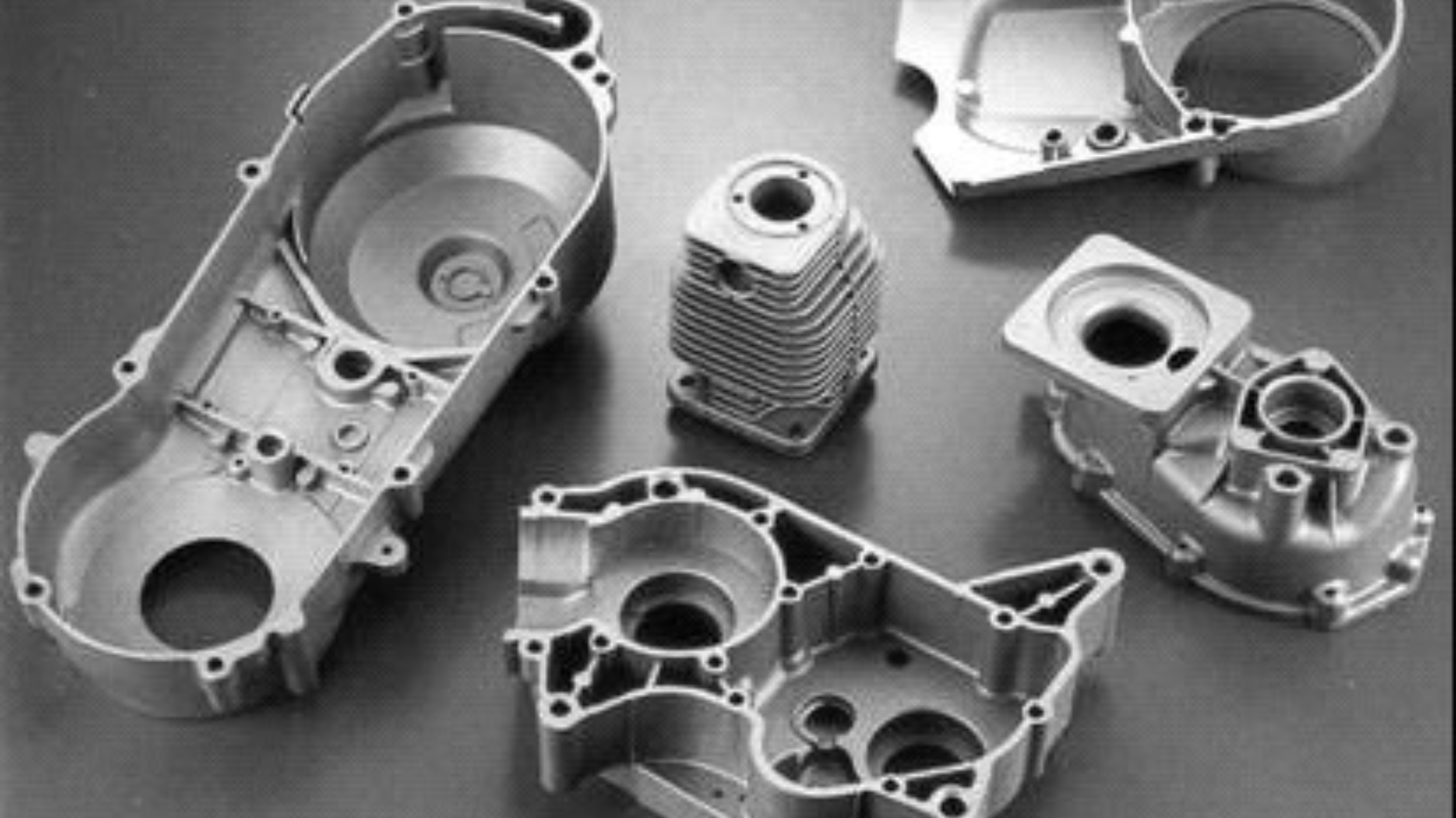 Disassembled aluminum engine parts, including a cylinder, a piston, and engine casings, laid out on a flat surface.