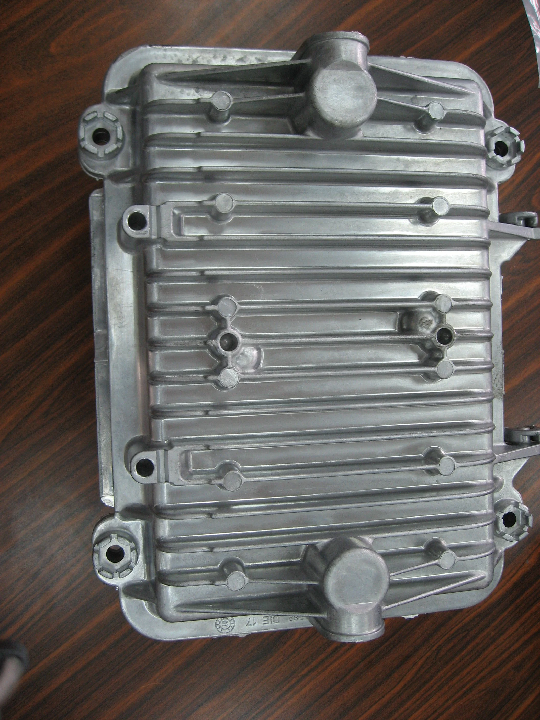 Metallic electronic component, possibly part of a machine or device, placed on a wooden surface.