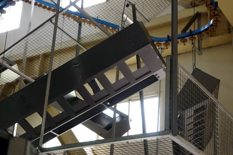 Interior view of a multi-story building with metal and wooden staircases and walkways, seen from below, with natural light coming through windows.