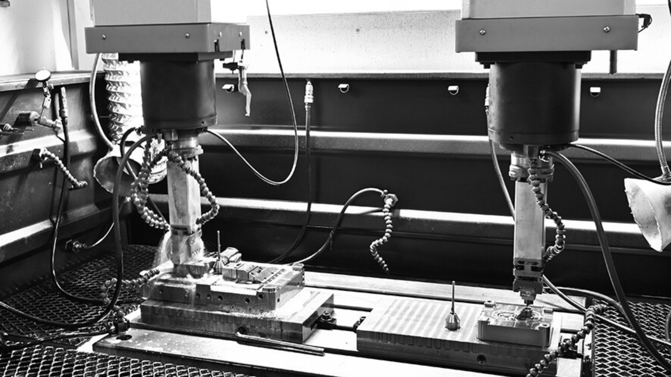 Black and white photograph of a laboratory setup with two mechanical devices connected by various hoses and wires, mounted on metal stands, with a grid metal surface underneath.
