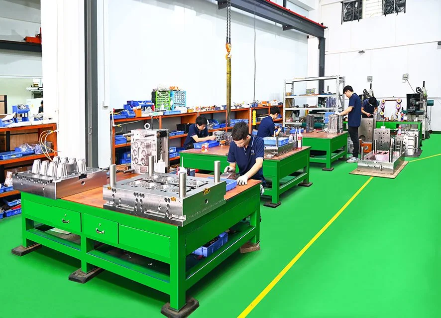 Factory workers assembling large metallic components at green workbenches in an industrial workshop.