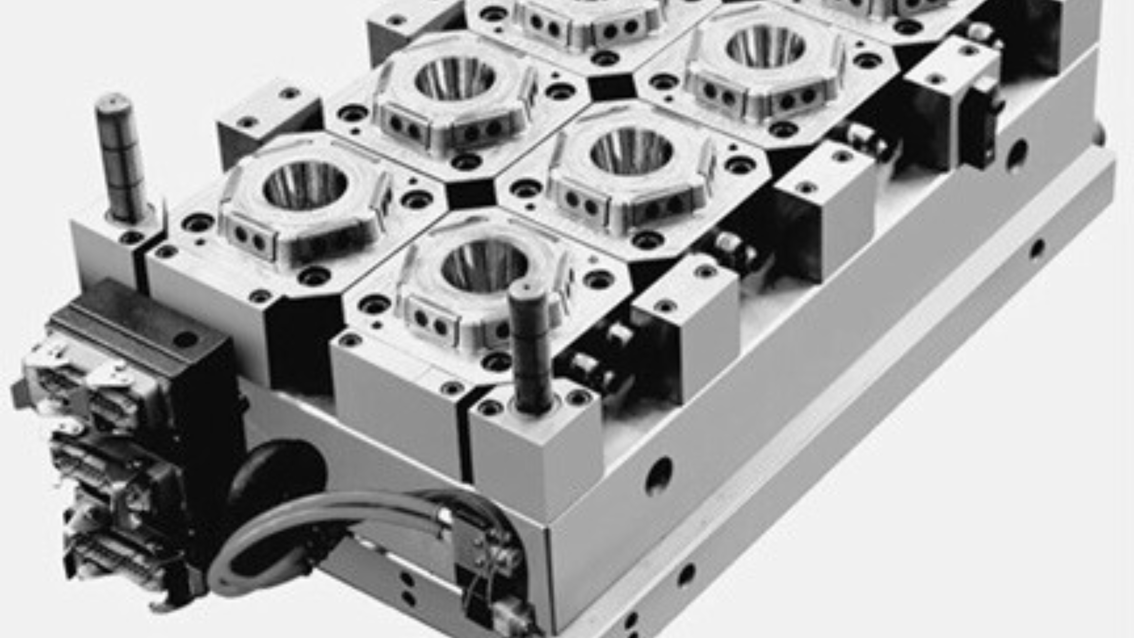 Black and white photograph of a mechanical part or machine component with several circular and rectangular features, mounted on a base with various screws and fasteners.