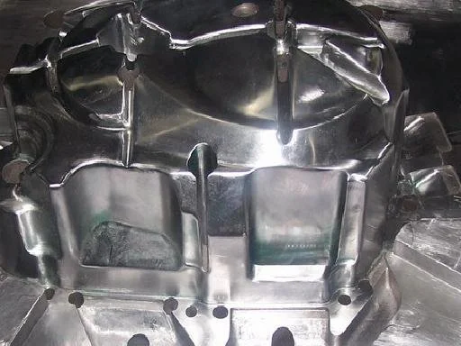 Close-up of a shiny, metallic engine component or mold with various indentations and raised sections.