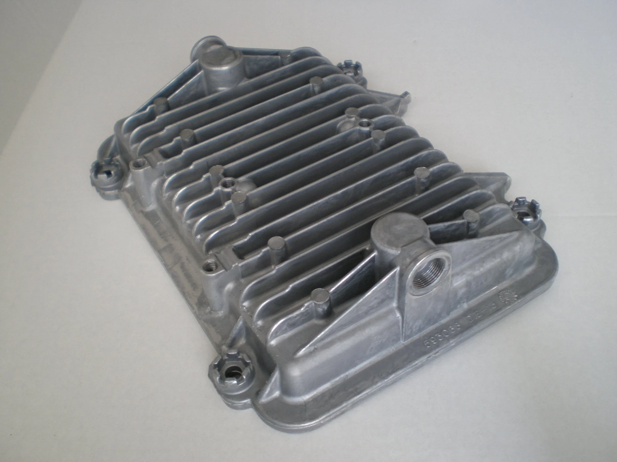 Metal engine component with fins and bolt holes on a white surface.