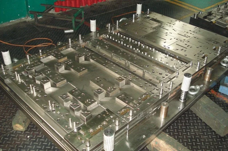 Close-up of a large metal mold or industrial manufacturing fixture with multiple components, screws, and fixtures on a black surface.