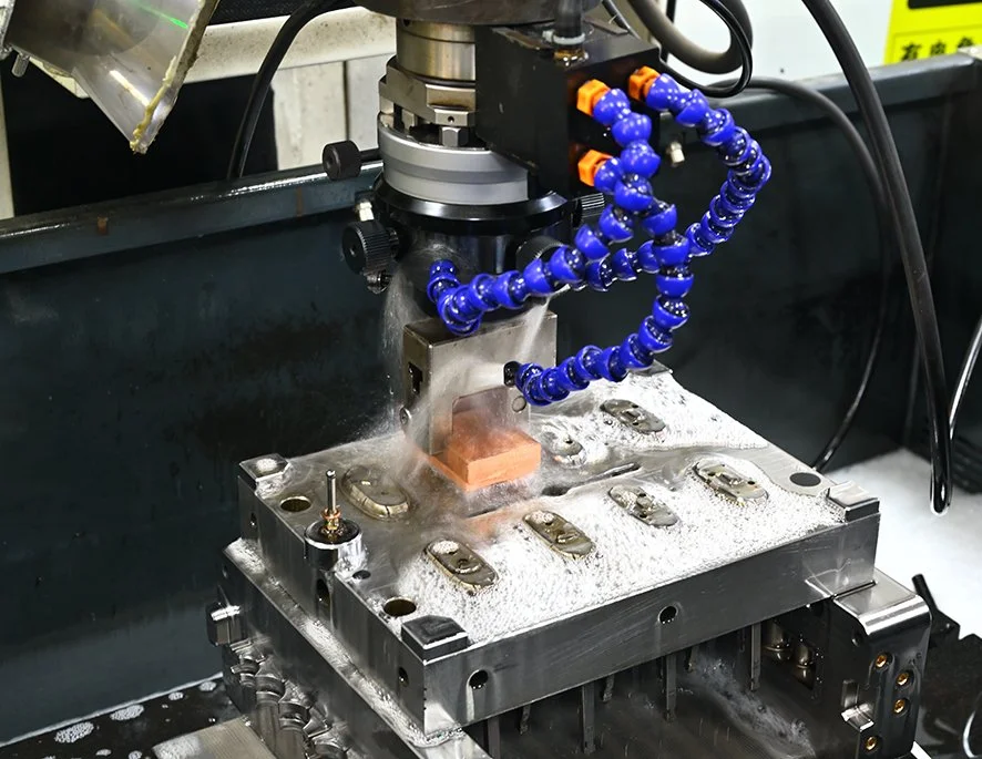 Close-up of a CNC machine drilling a metal workpiece, with coolant spray and flexible coolant hoses attached.