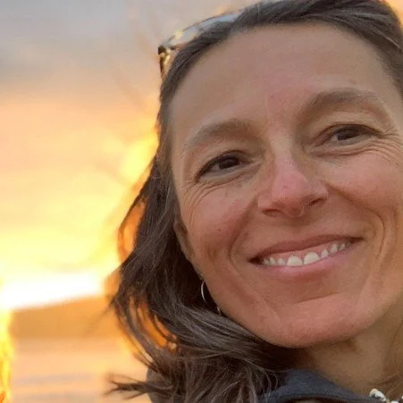 A woman smiling outdoors at sunset.