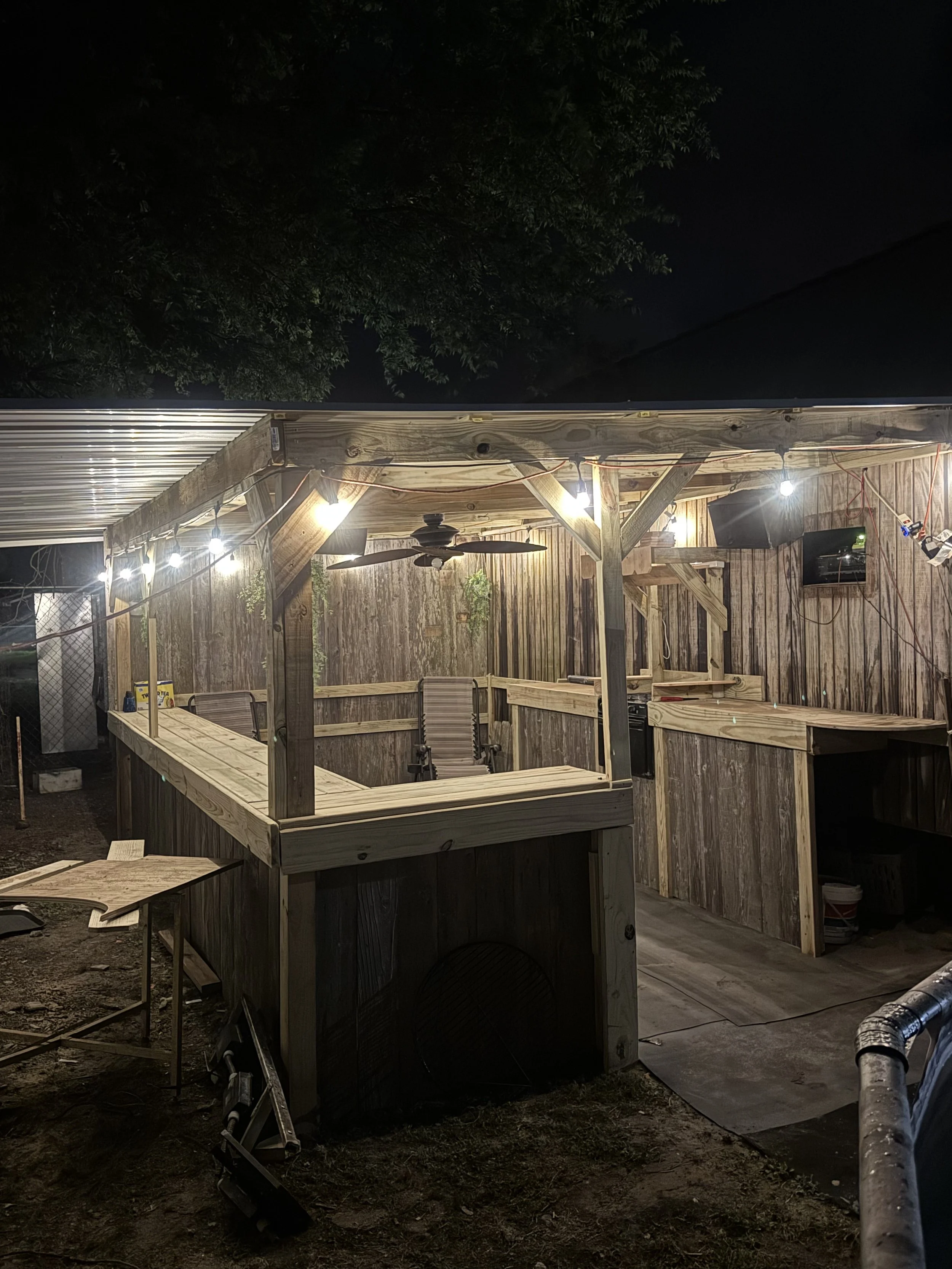 Nighttime outdoor bar or patio area with wooden framing, string lights, a ceiling fan, with a rustic finish