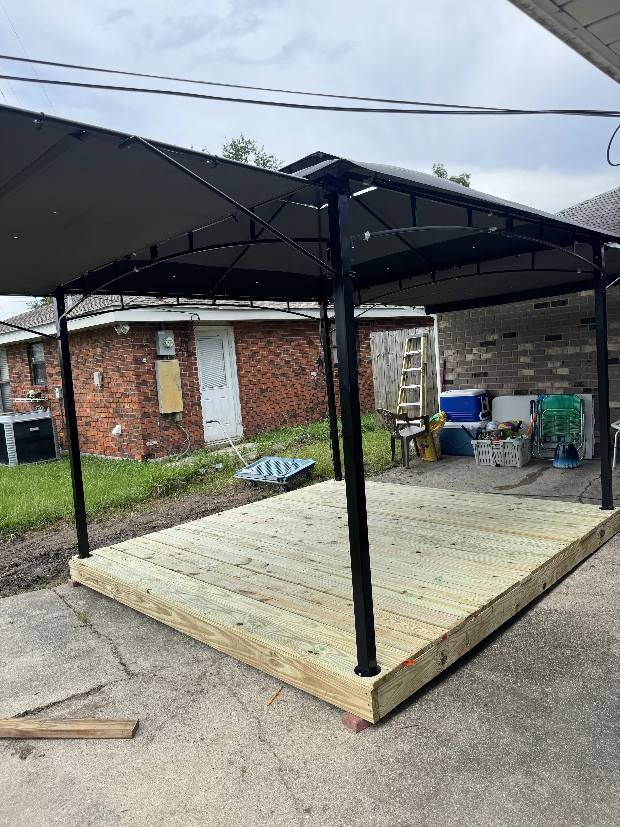 A newly built wooden deck with a black metal patio cover in a backyard