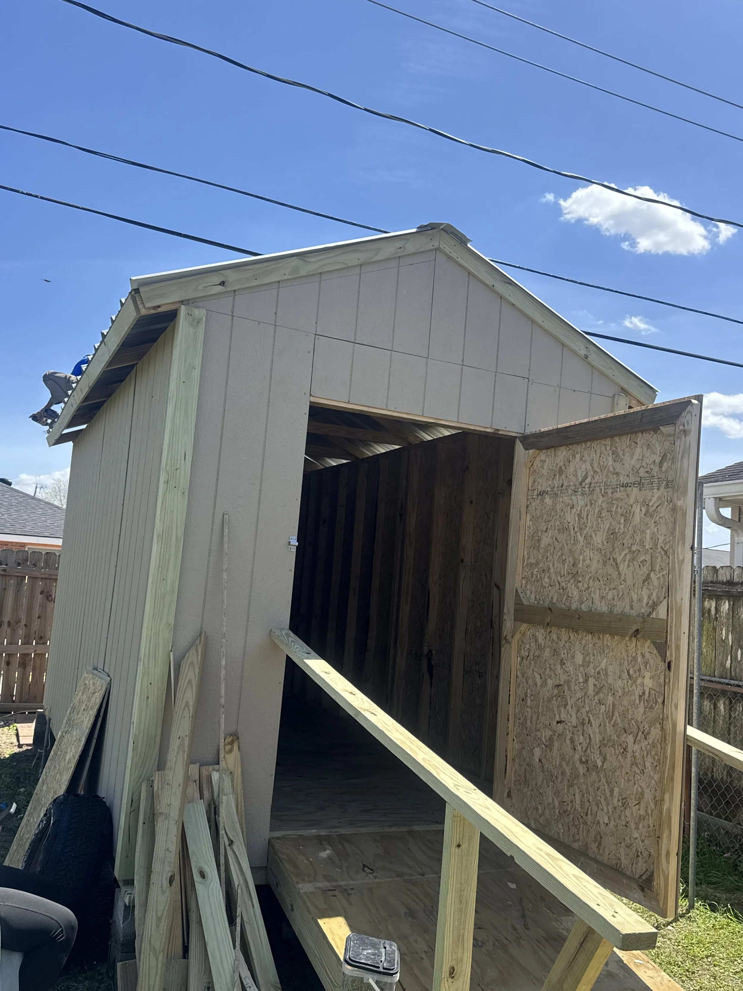 A small shed under construction with one side open, showing wooden framing
