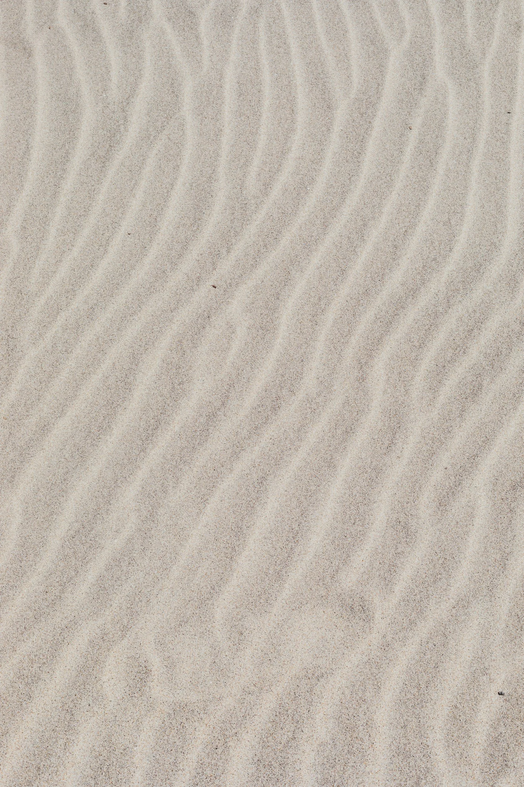Close-up of sand with gentle, wavy patterns formed by wind.