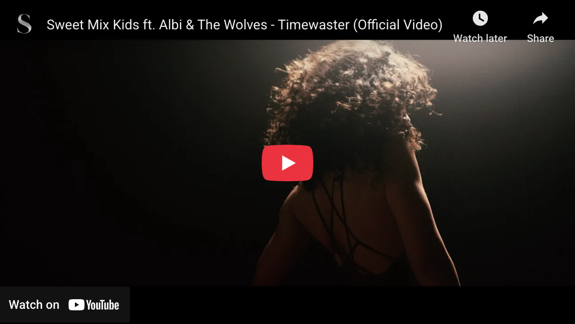 A woman with curly hair facing away, in a dark setting with light highlighting her hair and shoulders, for the YouTube video titled 'Sweet Mix Kids ft. Albi & The Wolves - Timewaster (Official Video)'.