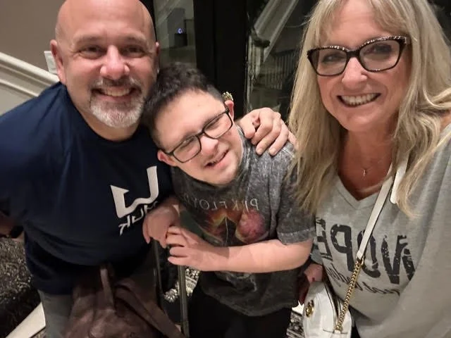 A happy family of three, a man, a woman, and a boy with intellectual disabilities, smiling and posing together indoor.