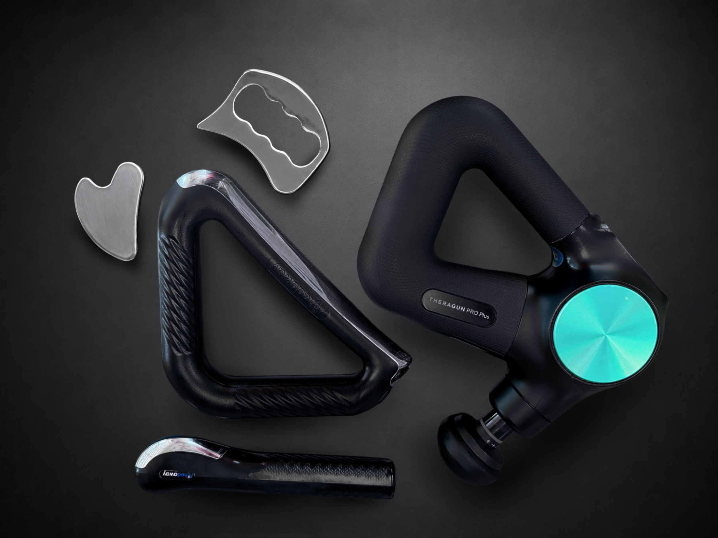 Massage gun and recovery scraping tools displayed on a dark surface.