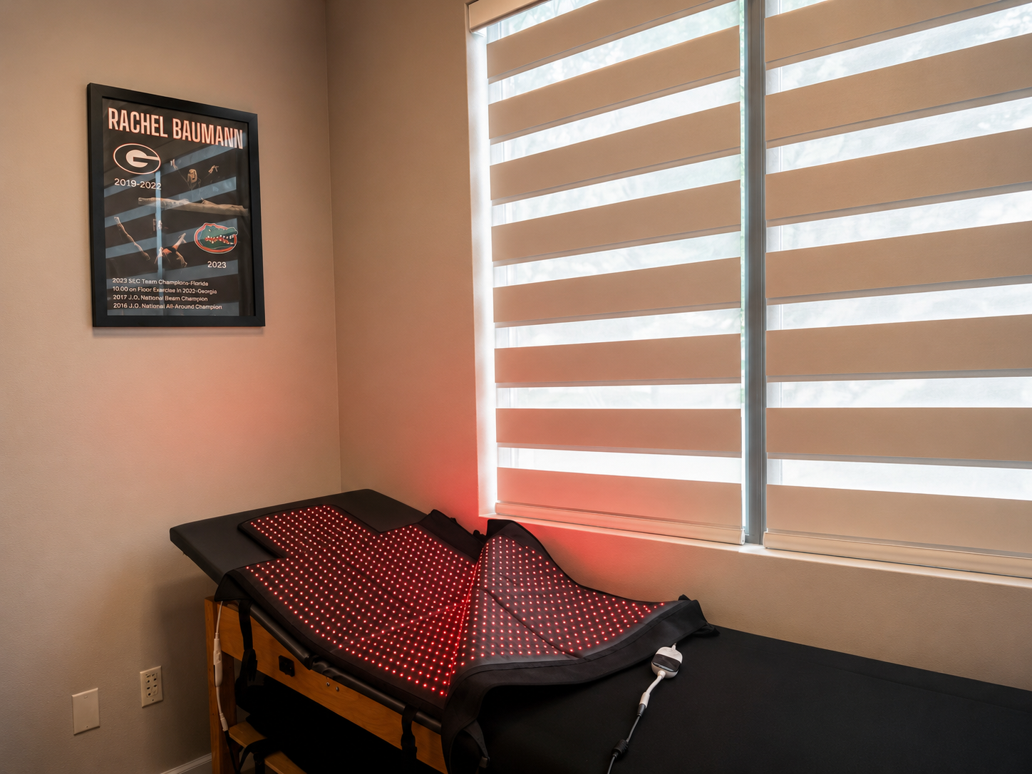Treatment table with red light therapy equipment positioned near large windows.