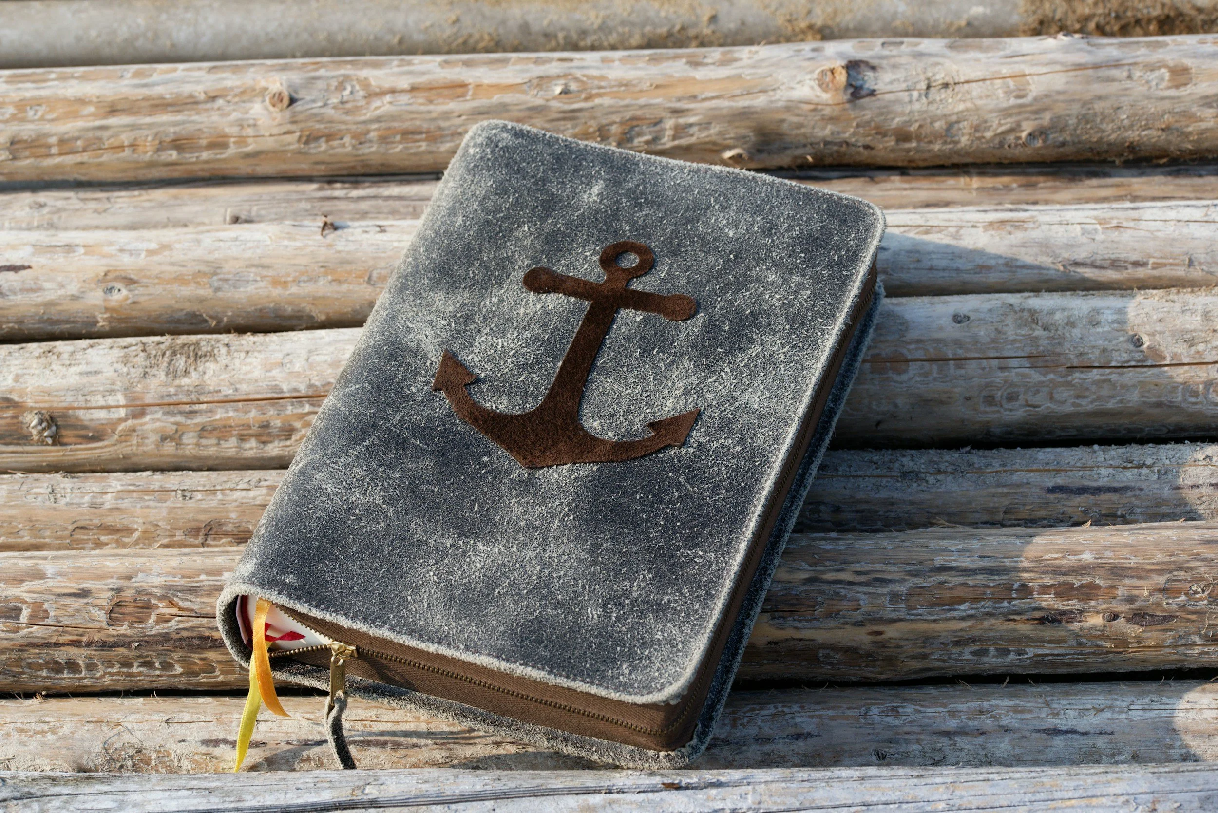 A closed notebook with a textured cover featuring a rusty anchor symbol, resting on weathered wooden planks.