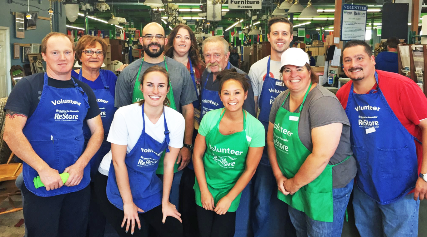 Group of volunteers in aprons smiling in a store or warehouse setting.