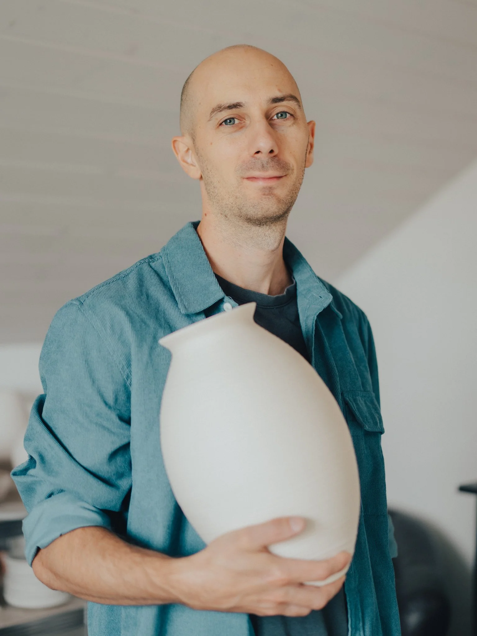A man with a bald head and blue eyes holding a large onion while standing indoors.
