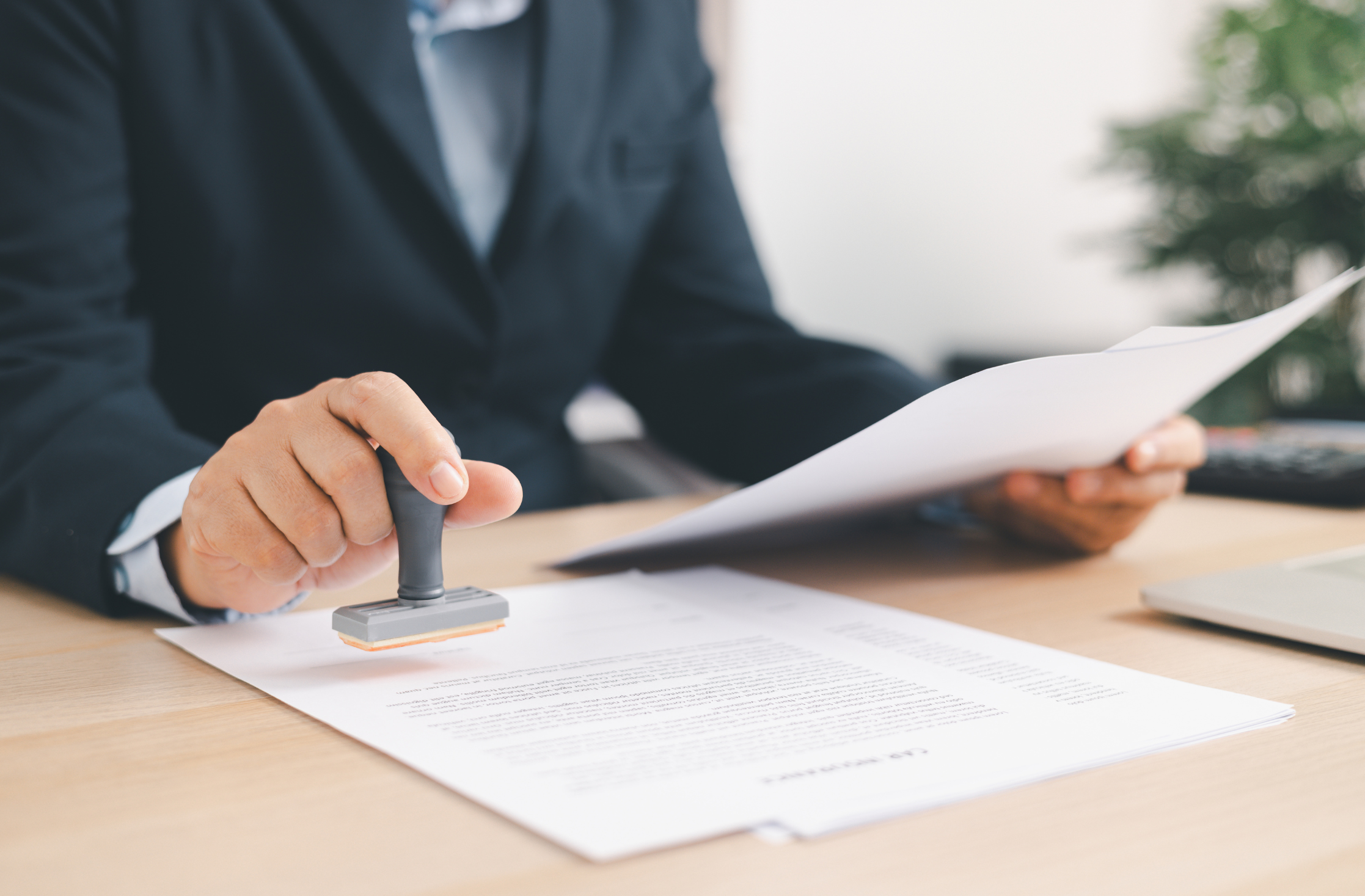 Person in a suit stamping a document on a wooden desk.