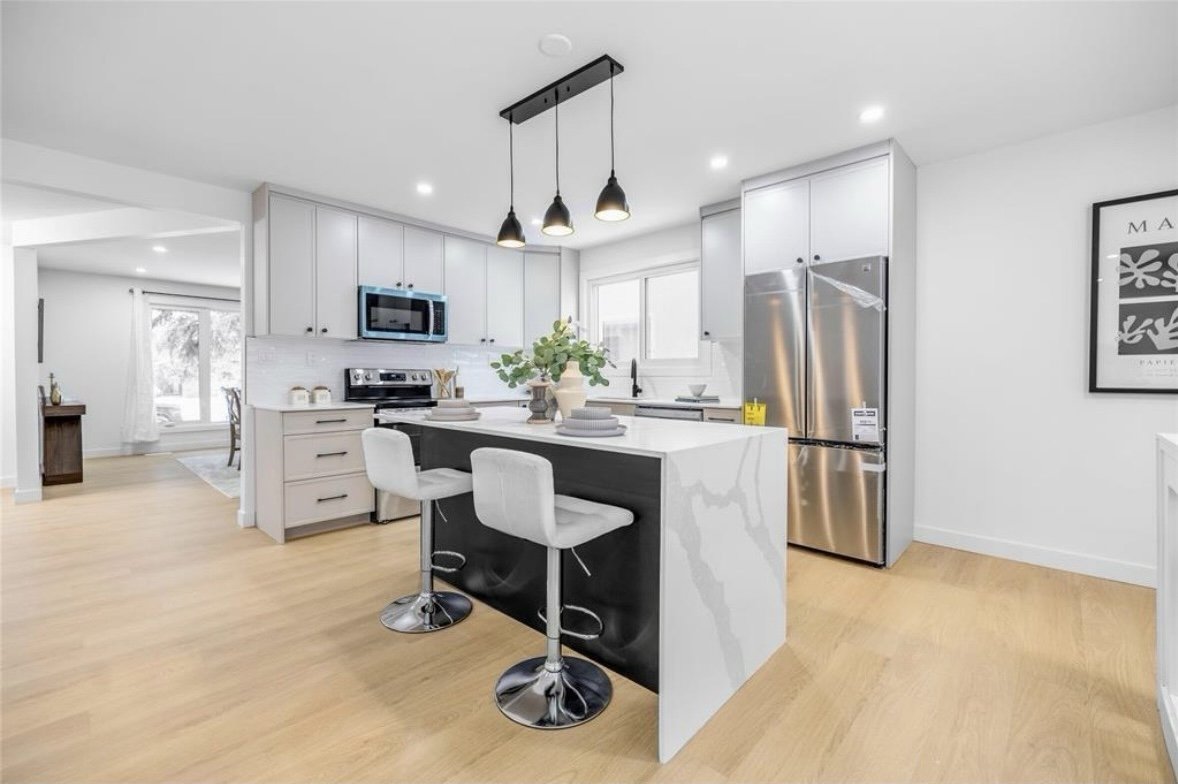 Modern white kitchen with a black and white island, stainless steel appliances, white cabinetry, and pendant lighting overhead.