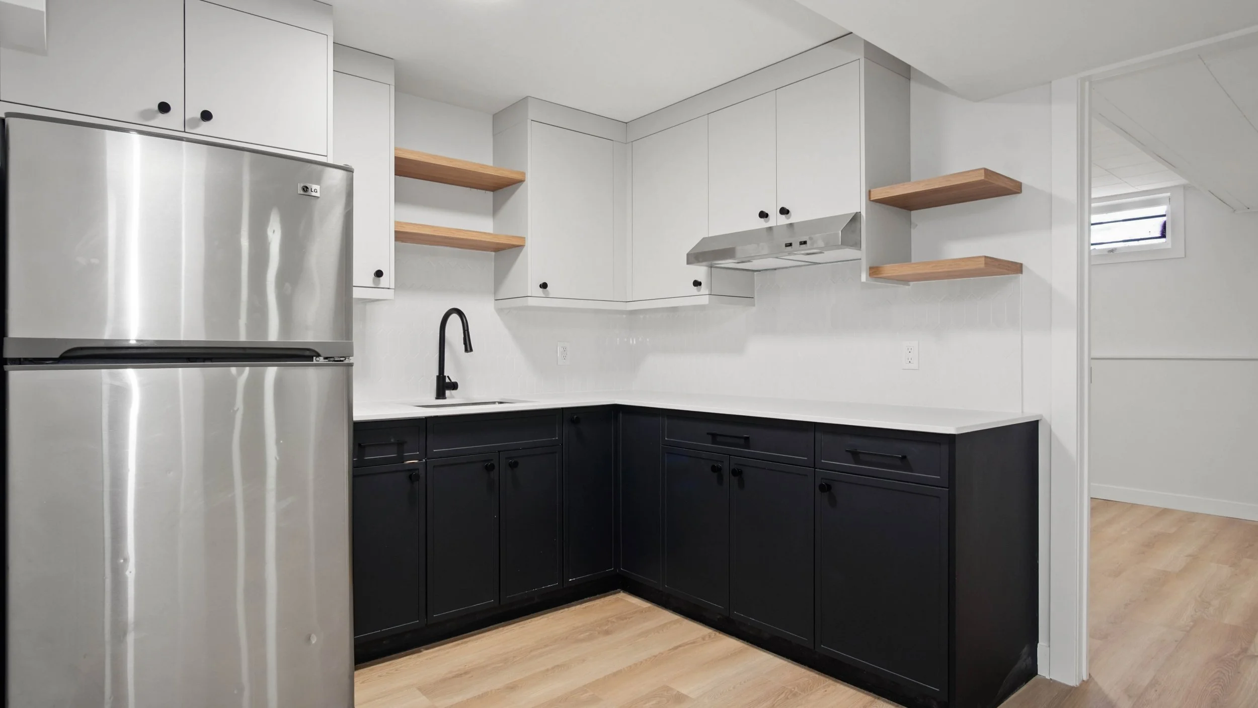Modern kitchen with black lower cabinets, white upper cabinets, wooden open shelves, stainless steel refrigerator, black faucet, and white countertops.