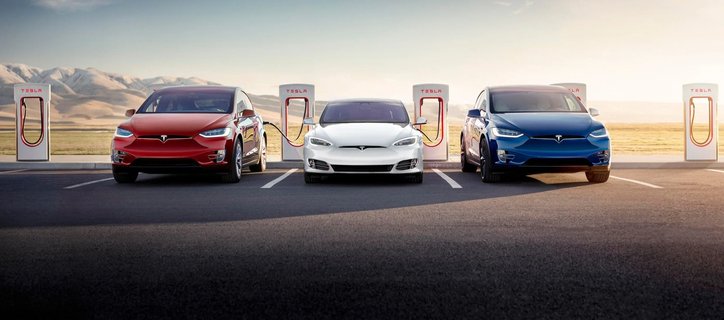 Three Tesla electric cars parked at charging stations outdoors, with two charging stations on either side and a white car in the middle, set against a mountainous landscape at sunset.
