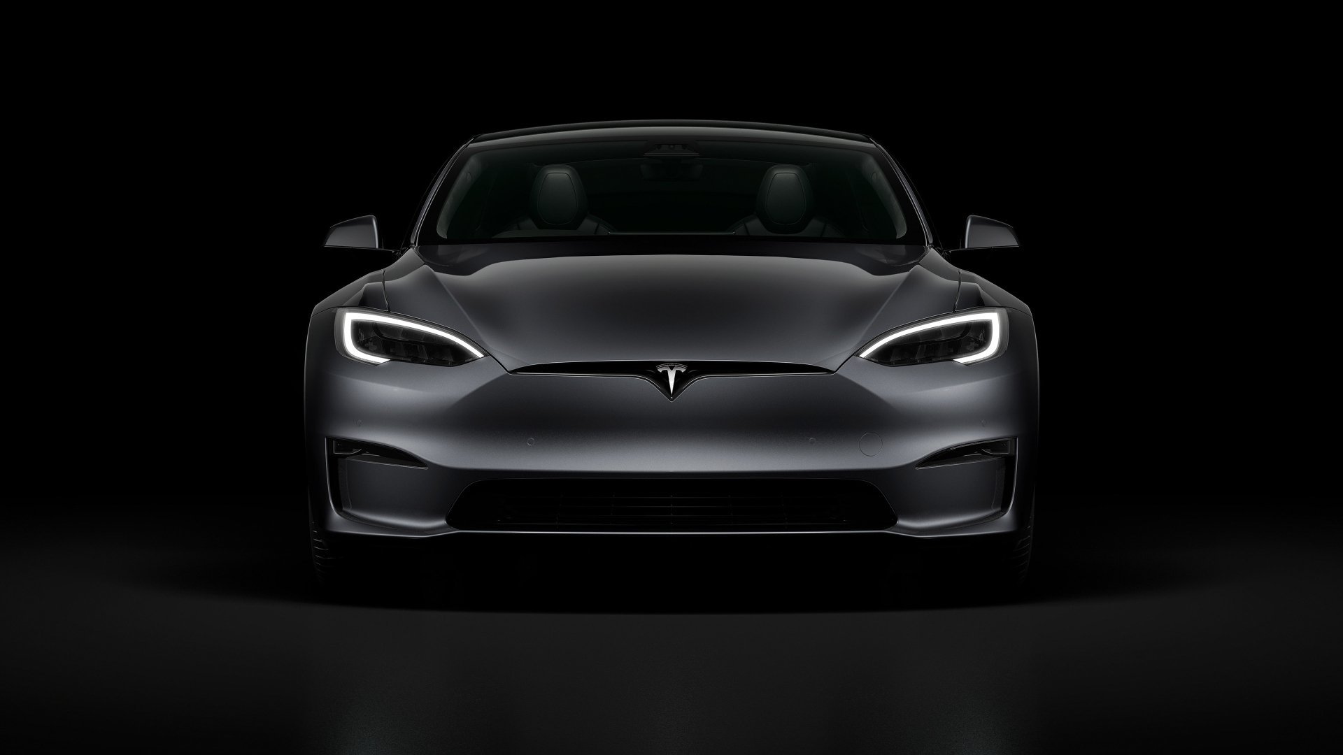 Front view of a sleek black Tesla electric car against a dark background.