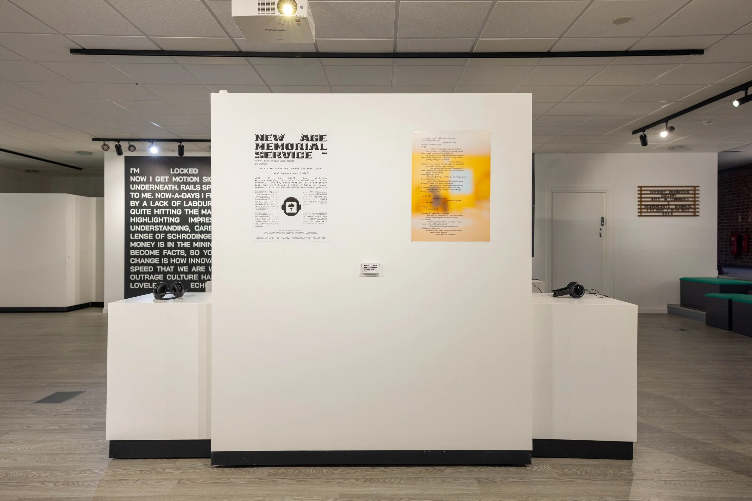 Art exhibit in a gallery with white walls, displaying texts and images, with headphones on pedestals and modern lighting.