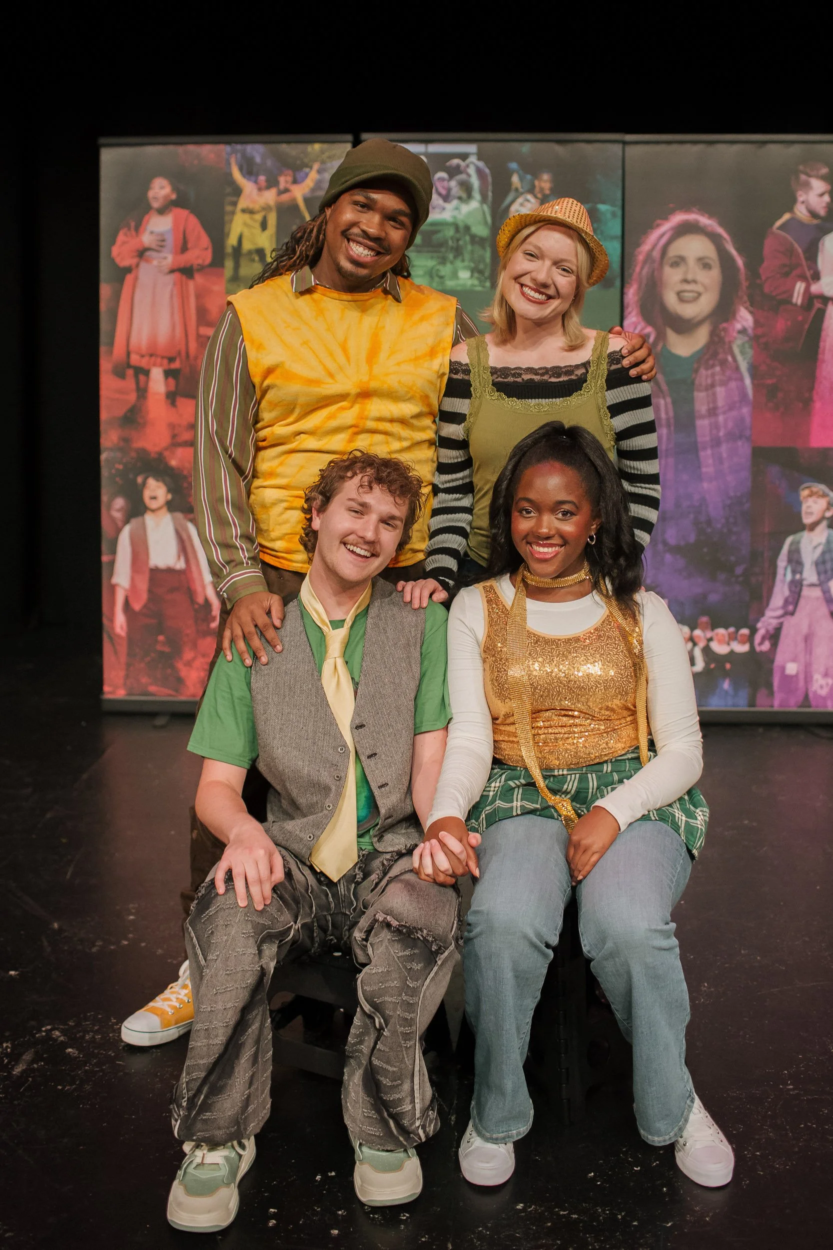 Group of five young actors on stage, smiling and posing in front of a colorful theatrical backdrop.