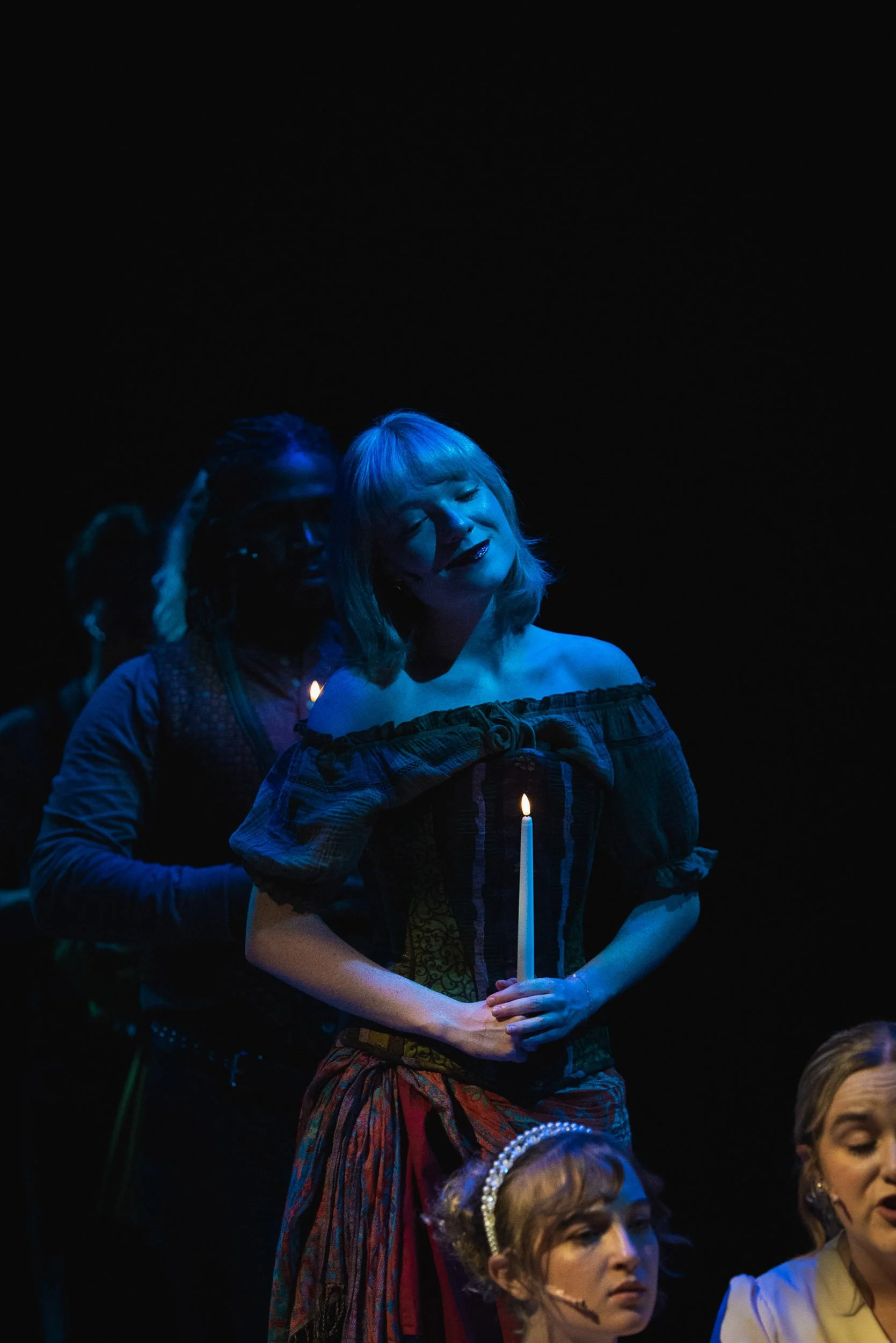 Actress Olivia Scott in a period costume holding a lit candle during a theatrical performance or reenactment.