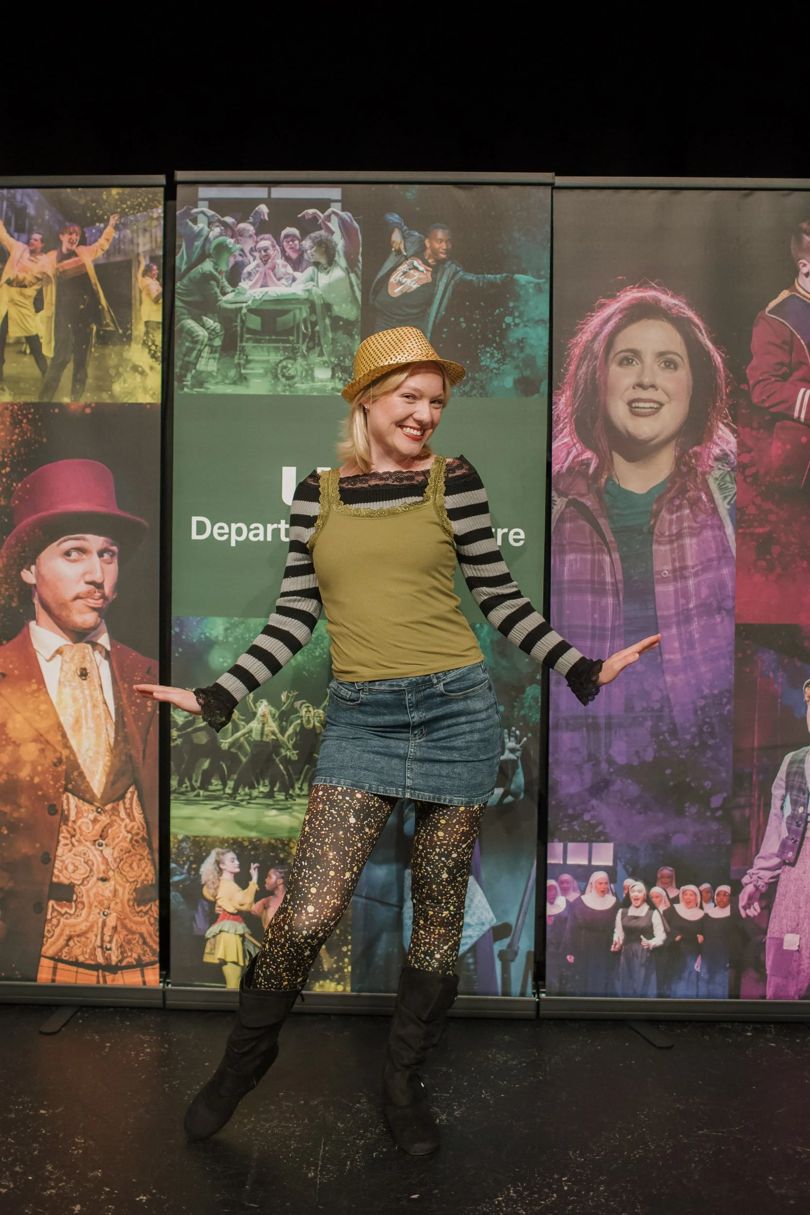 A woman smiling and dancing in front of theater posters at a stage or event.